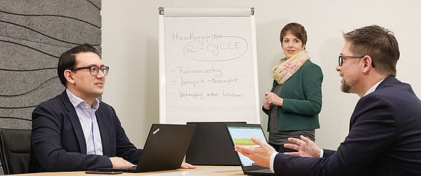 Drei Professionals diskutieren über ein Thema vor einem Whiteboard