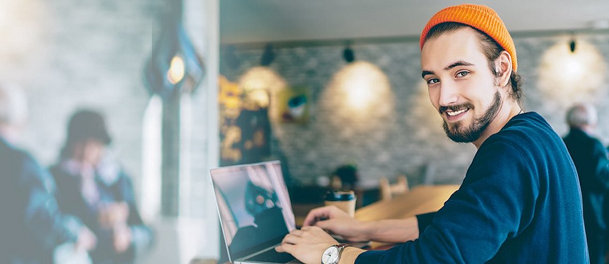 Ein junger Mann sitzt vor einem Laptop im Café