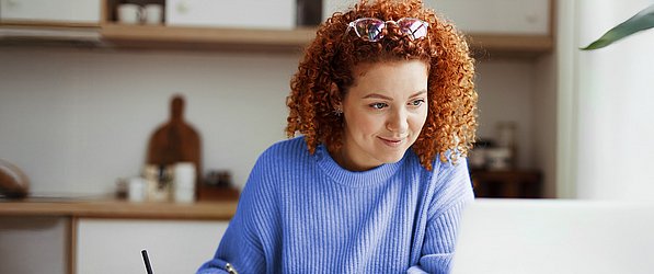 Shopper Experience Studien Eine rothaarige Junge Frau vor einem Laptop beim Lernen