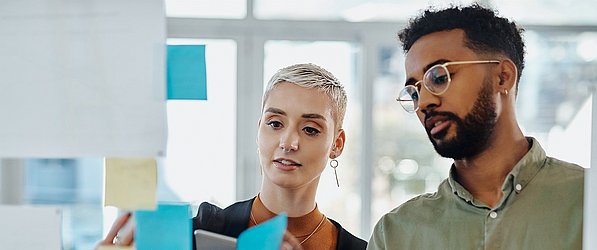 Beratung im Bereich Shopper Experience Eine Business-Trainerin mit einem jungen Mann vor einer Glaswand mit Post-its