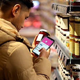 Ein Mann scannt mit der SoVi App auf seinem Handy im Supermarkt Marmelade.