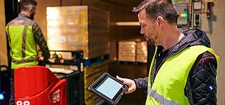 Lagermitarbeiter checkt digitalen Lieferschein uaf Tablet, im Hintergrund wird LKW beladen