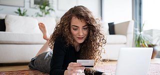 Frau vor Laptop beim Onlineshopping mit Kreditkarte in der Hand