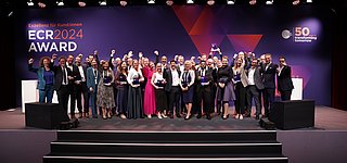 Gruppenbild der jubelnden Gewinnerteams vom ECR Award 2024 auf großer Bühne mit Trophäen