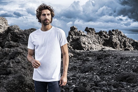 Ein Bild von einem Mann vor einer Felsenlandschaft mit einem weißen T-Shirt von promodoro