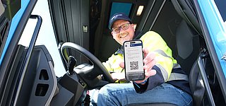 Fahrer zeigt aus LKW-Kabine digitalen Lieferschein auf Smartphone