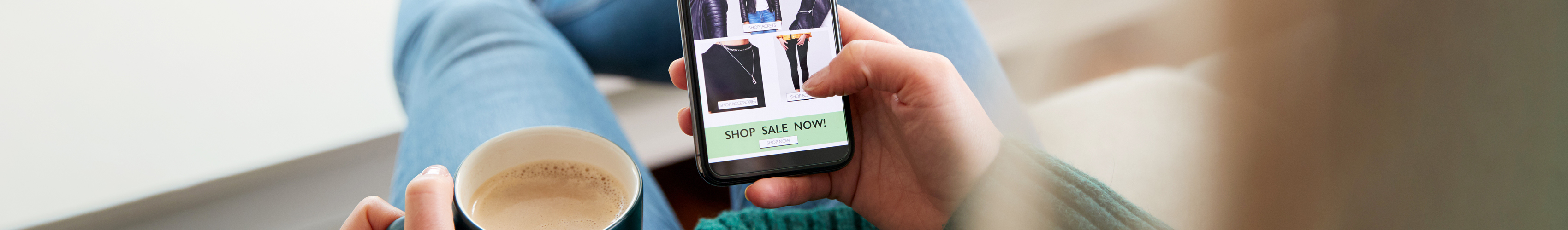 Shopper sitzt bequem auf einem Sofa und scrollt auf dem Smartphone durch einen Mode Onlineshop