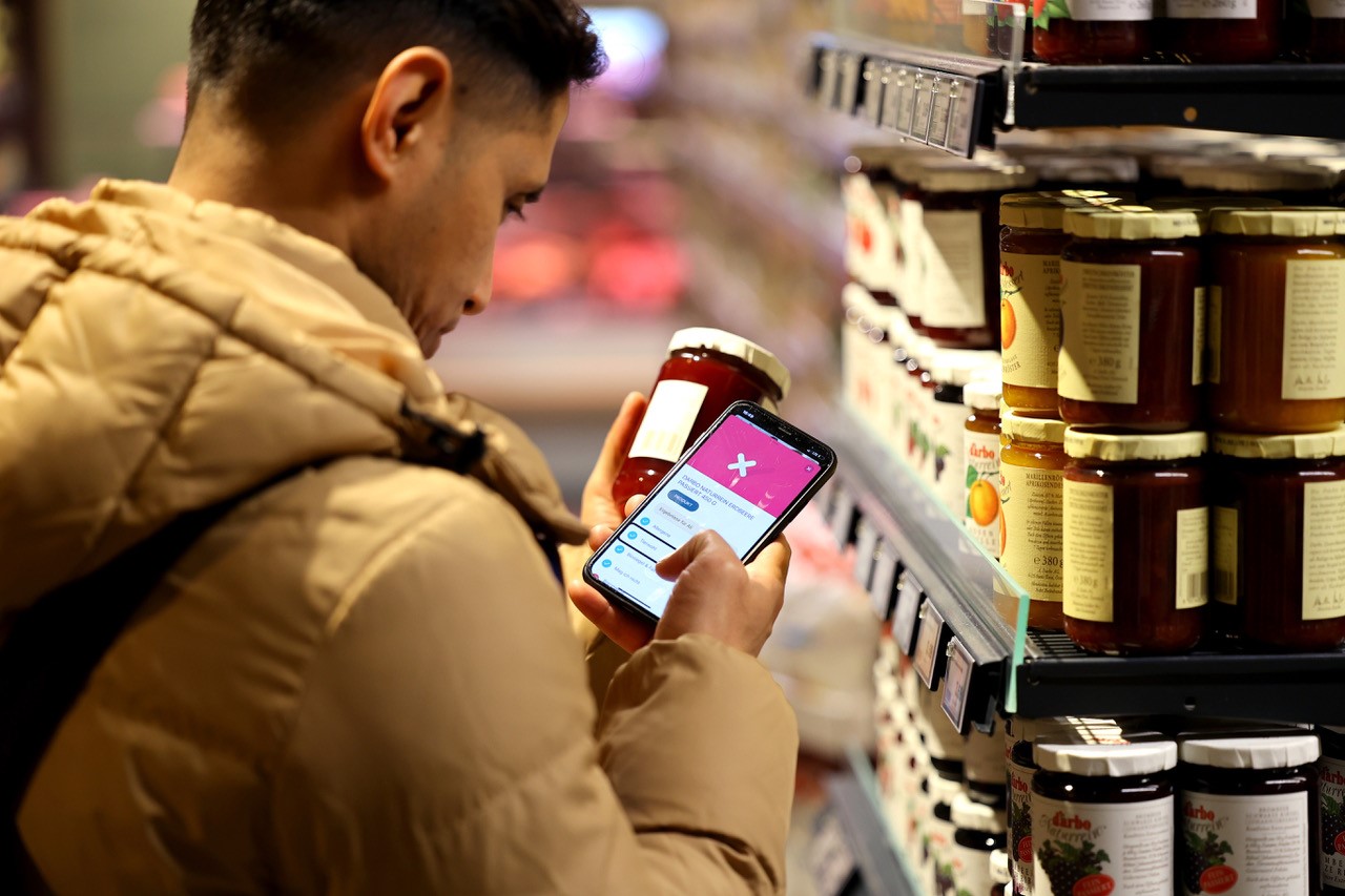 Ein Mann scannt mit der SoVi App auf seinem Handy im Supermarkt Marmelade.